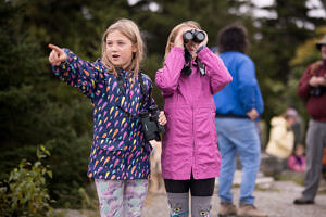 Two girls watch for hawks, one pointing and one using binoculars. (photo © Ben Conant)