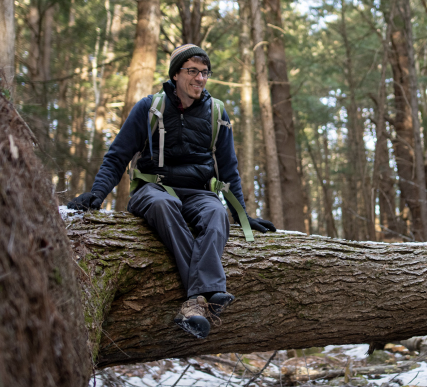 John Benjamin sits on a fallen tree in the forest. (photo © Ben Conant)