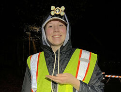 Taylor Jackson stands on a road at night, wearing a reflective vest and headlamp. (photo © Brett Amy Thelen