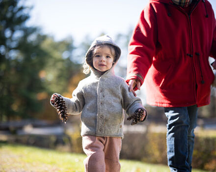 A toddler holds a pinecone in her hands. (photo © Ben Conant)