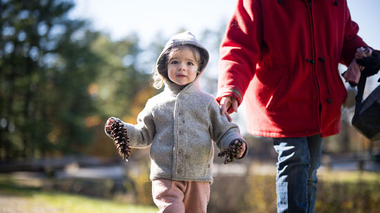 A toddler holds a pinecone in her hands. (photo © Ben Conant)