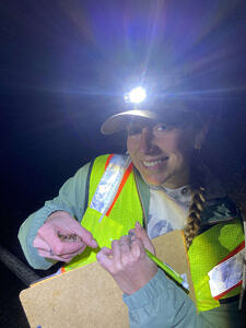 Veronica Kroha smiles while holding a wood frog in one hand and a clipboard in the other. (photo © Taylor Jackson)