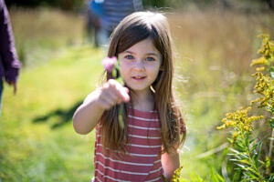 A young girl holds a small flower while standing in a sunny field. (photo © Ben Conant)