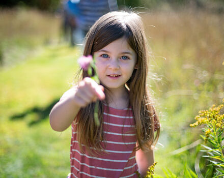 A young girl holds a small flower while standing in a sunny field. (photo © Ben Conant)
