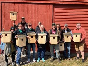 A team of volunteers from M&T Bank stands outside a red barn holding kestrel next boxes that they helped to build. (photo © Phil Brown)