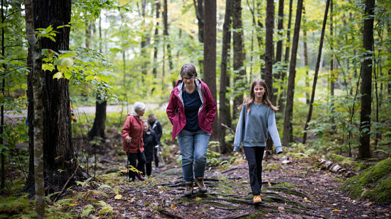 A mother and daughter hike through the woods, with other hikers visible in the distances. (photo © Ben Conant)