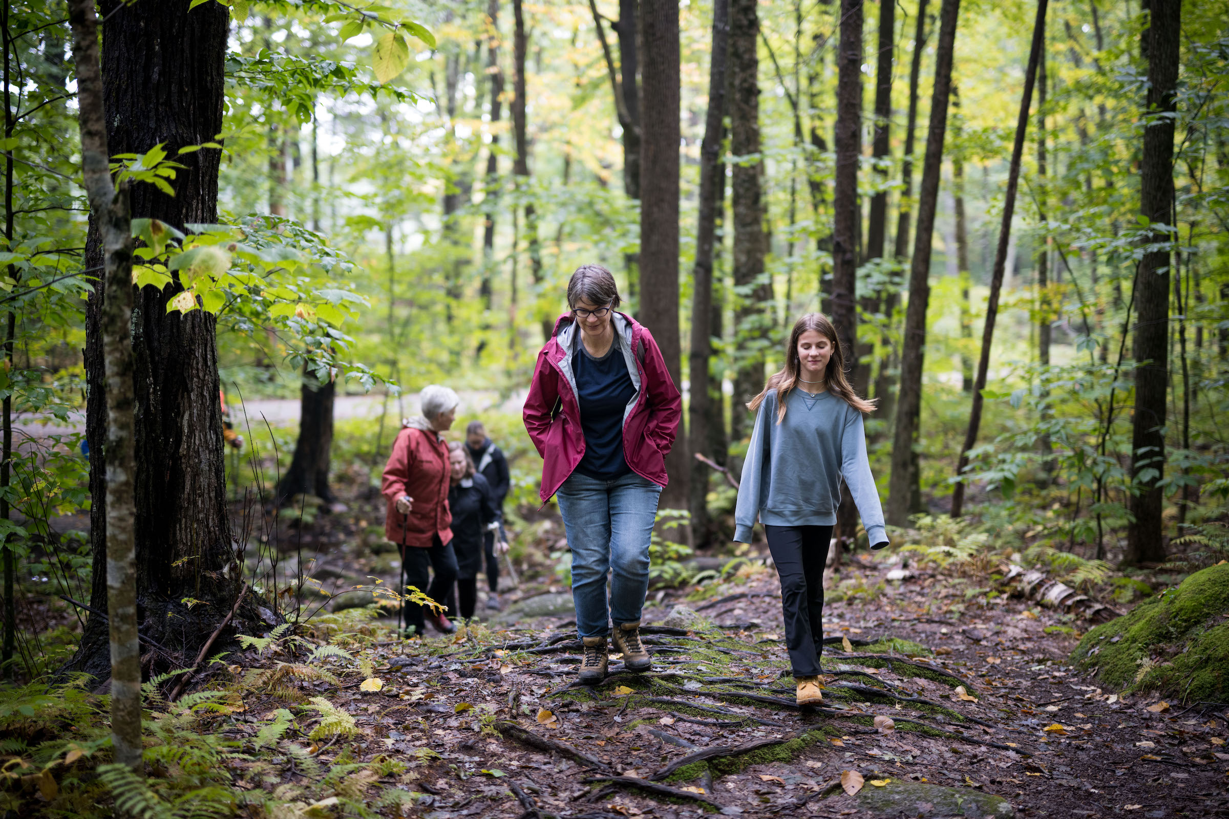 A mother and daughter hike through the woods, with other hikers visible in the distances. (photo © Ben Conant)