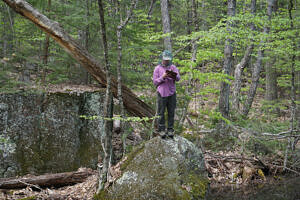 Wyatt Ferrando stands on a boulder in the forest, writing on a clipboard. (photo © Donta Selden)