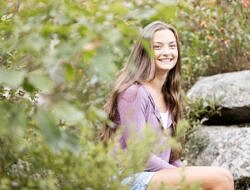 Irini Stefanakos smiles while sitting on a stone wall, surrounded by greenery.