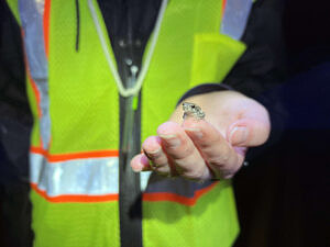 A person wearing a reflective vest holds out their hand, with a very tiny gray tree frog perched on the tip of their pointer finger. (photo © Brett Amy Thelen)