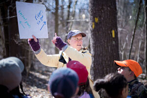 Kara Reynolds holds a sign while teaching students in the woods. (photo © Ben Conant)