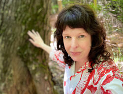 Michelle Aldredge smiles while touching a tree.
