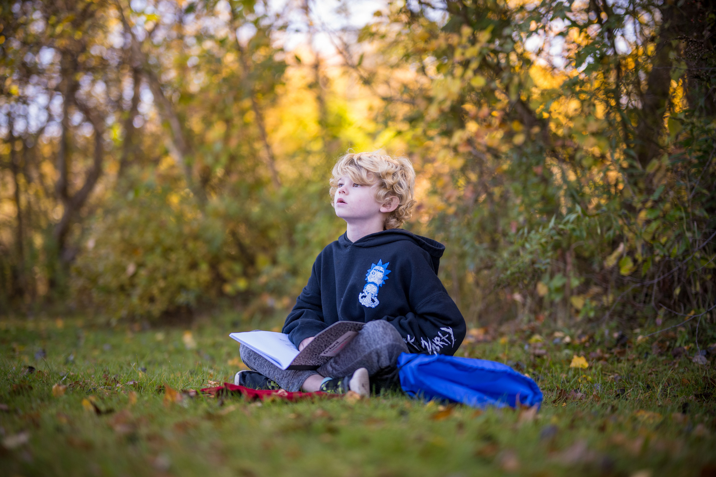 A boy sits in the autumn woods looking up, with a nature journal in his lap. (photo © Ben Conant)
